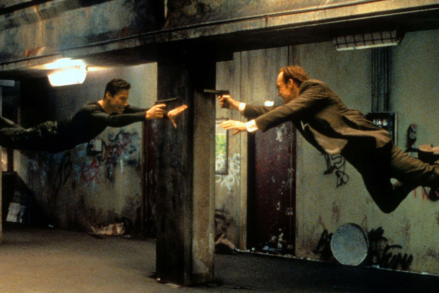 کیانو ریوز و هیوگو وی‌وینگ در صحنه‌ای از فیلم ماتریکس (1999) اسلحه‌های خود را به سوی همدیگر نشانه گرفته‌اند